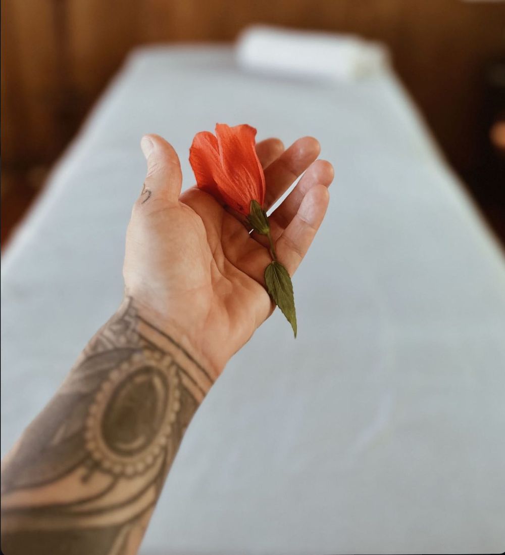 Mão tatuada segurando uma flor de hibisco sobre a maca